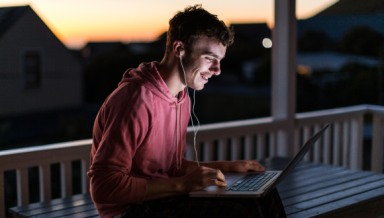 Young man on laptop with earphones, outside in the early morning.