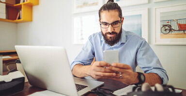 Man looking at a phone with a laptop next to him