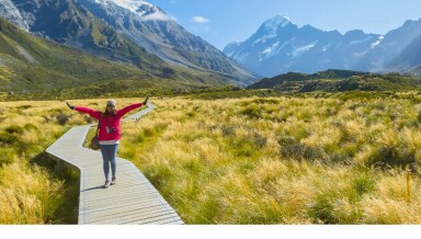 A girl with outstretched arms, posing for a photo on a track in the South Island.