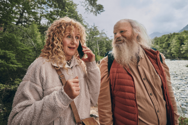 Couple walking beside a river in a forest while talking on a smartphone during an outdoor adventure.