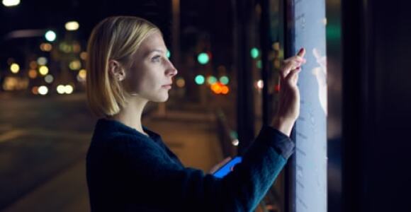 Young woman looking at a digital timetable at a bus stop