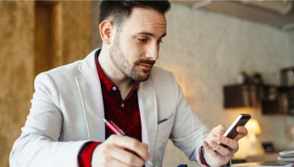 A man looking at his mobile phone and writing