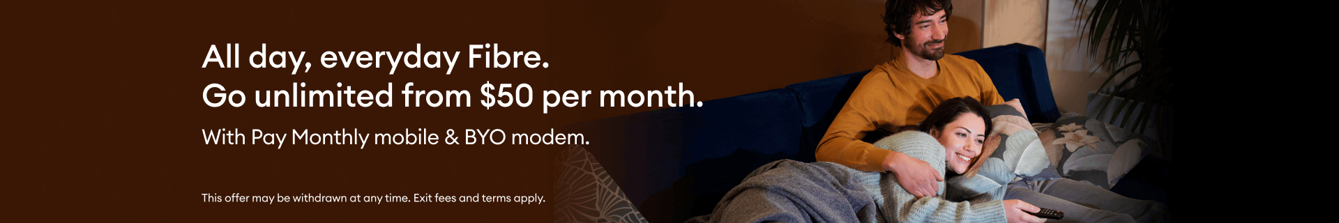 A couple snuggling on a couch, watching TV over fibre broadband.