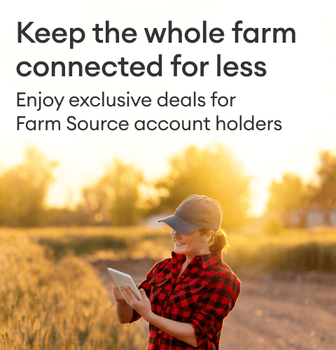 A farmer standing in a sunlit field and using a tablet.