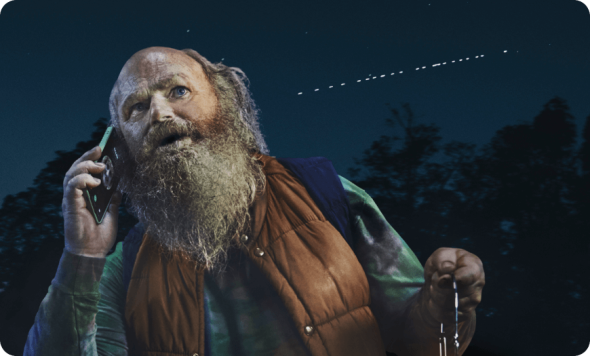 Man outdoors at night using a mobile phone and looking up at lights in the sky.