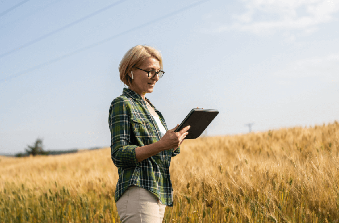 Lady wearing earbuds using a tablet in a crop field.