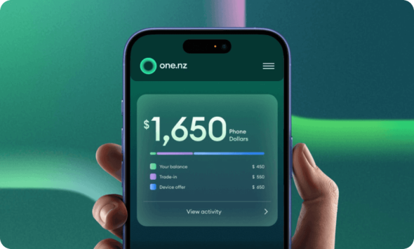 Hand holding a smartphone displaying the One NZ app with a phone balance and trade-in offer screen.