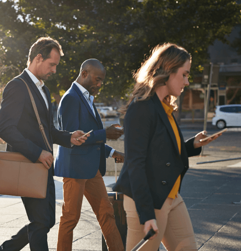 3 people walking on the street looking at their phones
