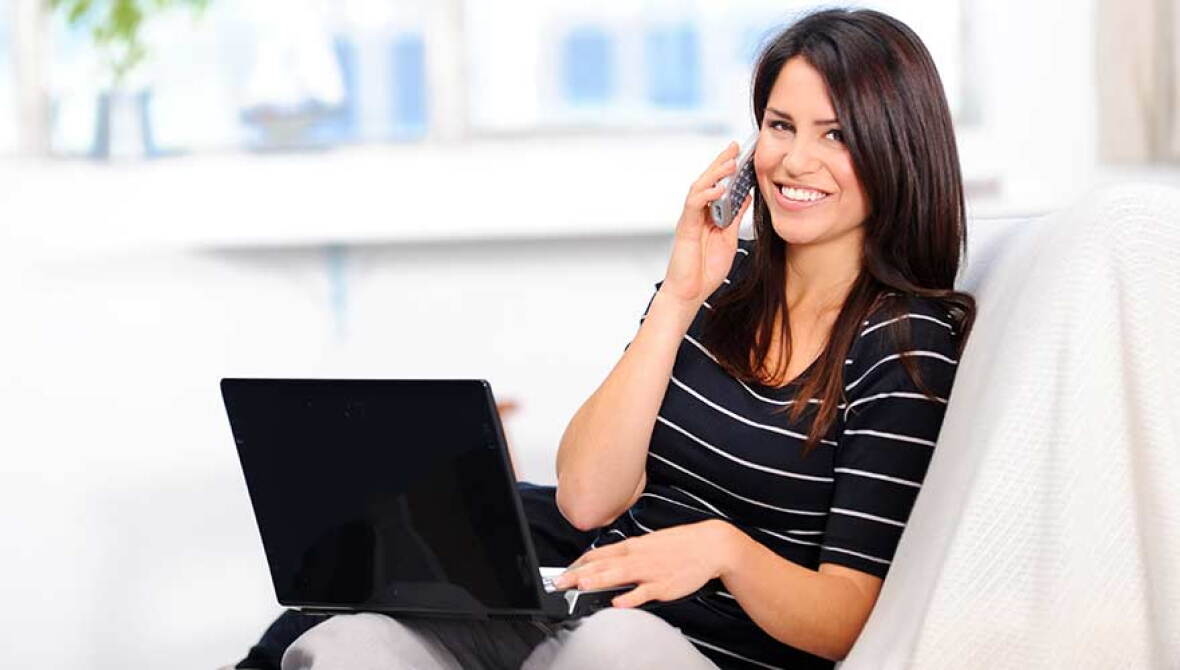 Woman in striped shirt talking on the phone and using a black laptop