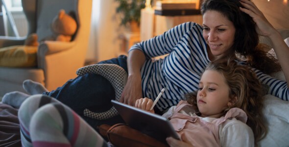 young girl using digital tablet while her mother looking at it.