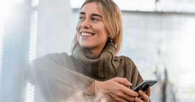 Person in knitted sweater holding smartphone indoors with soft lighting.