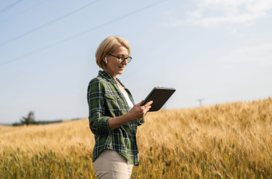 Lady wearing earbuds using a tablet in a crop field.