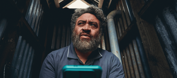 Man using a smartphone in a dimly lit rustic shed