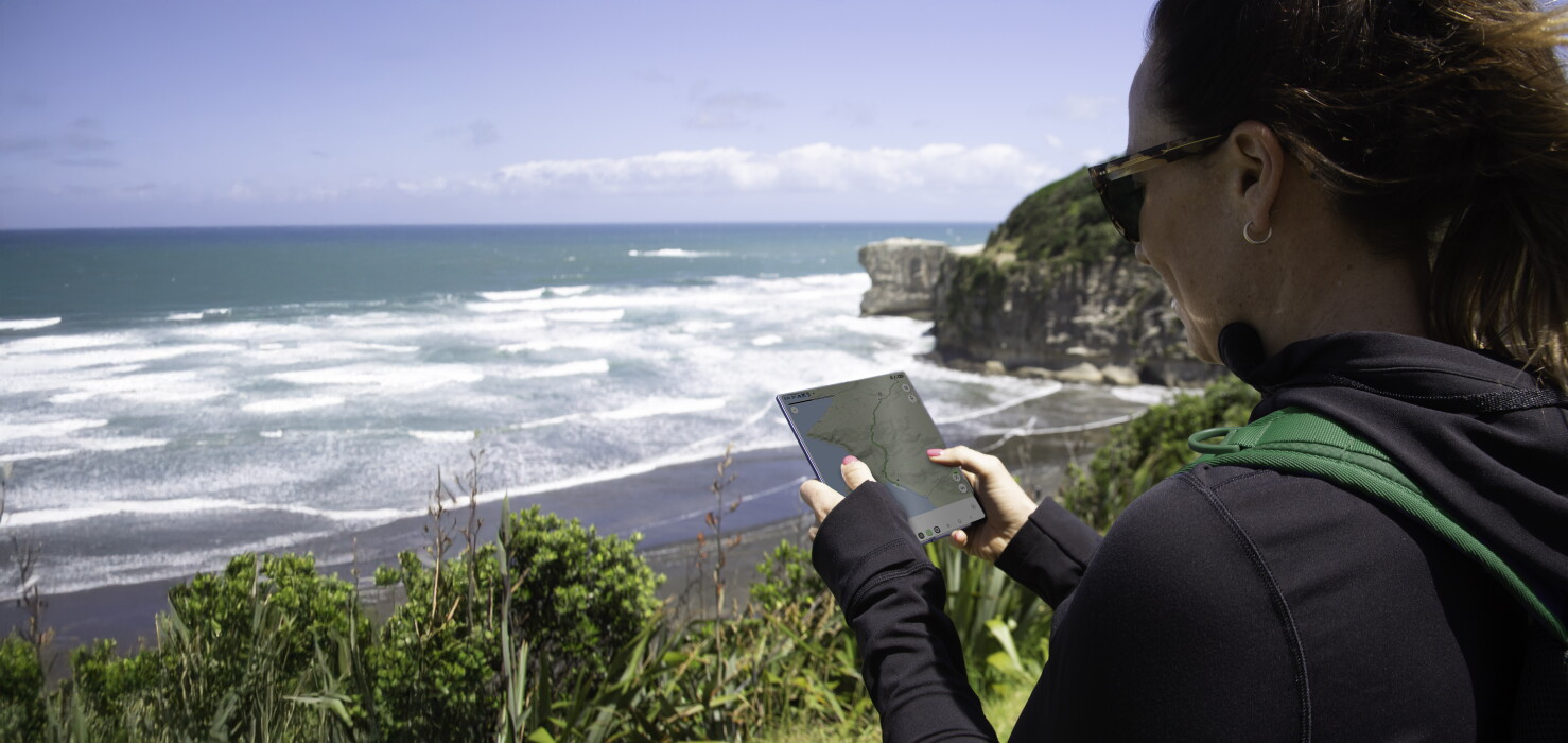 A lady using her phone at a remote beach location with One NZ.