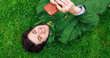 Person lying on grass using a red smartphone outdoors.