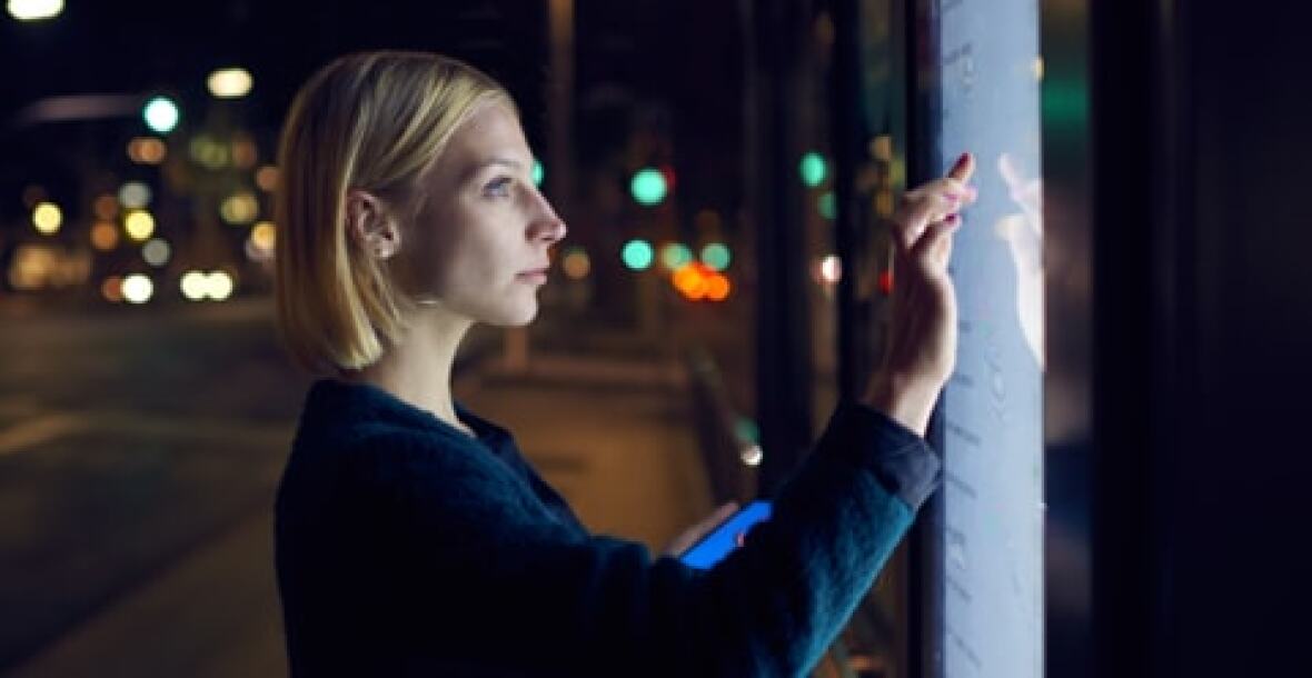 Young woman looking at a digital timetable at a bus stop