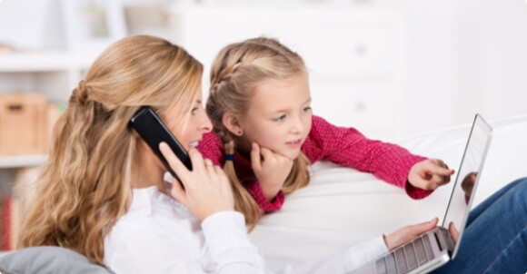 A woman on her phone while her daughter looking at their laptop.