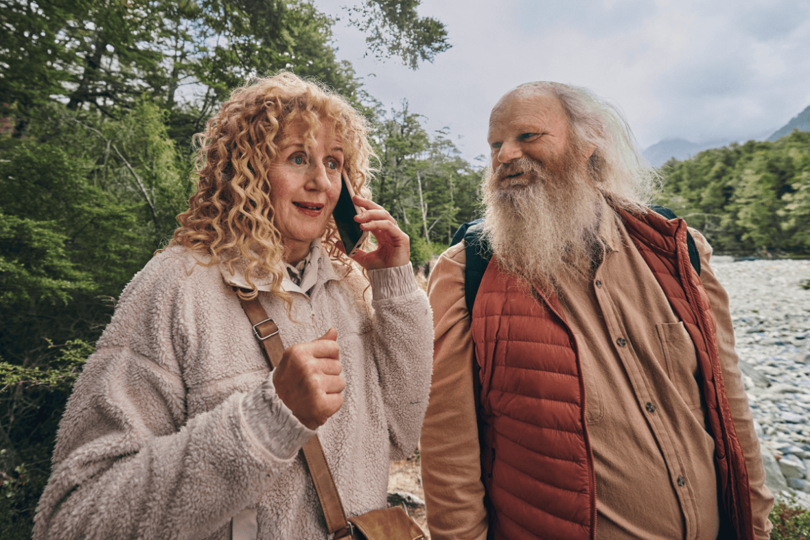 Couple walking beside a river in a forest while talking on a smartphone during an outdoor adventure.