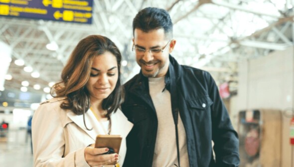 Man and woman looking at a mobile phone at an airport.