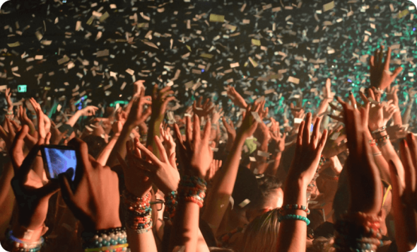 Crowd at a live concert with raised hands and confetti falling over the audience.