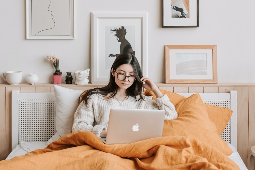 A woman, relaxed on her bed, using a MacBook laptop.