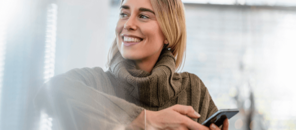 Person in knitted sweater holding smartphone indoors with soft lighting.