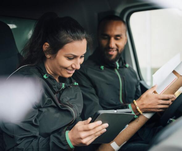 Two delivery drivers in a van, checking their delivery orders.