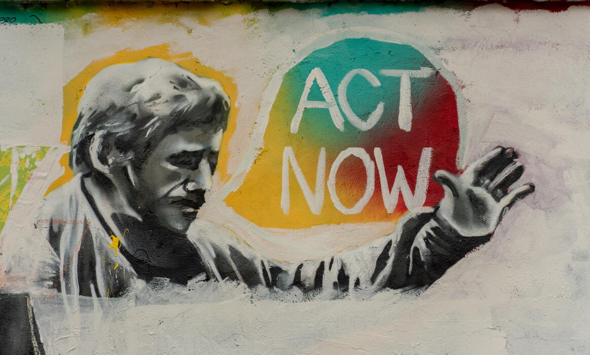 A graffiti wall featuring a greyscale man with a tri-colour speech bubble saying "ACT NOW" | Photo by Rod Long on Unsplash