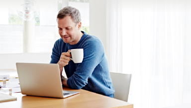 A man drinking from his white cup while looking at his laptop