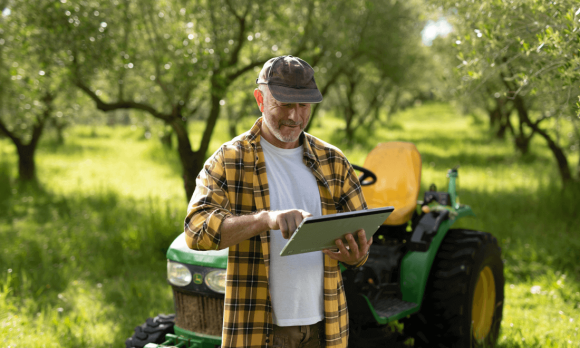 An orchard farmer, checking stats with his iPad, outside.
