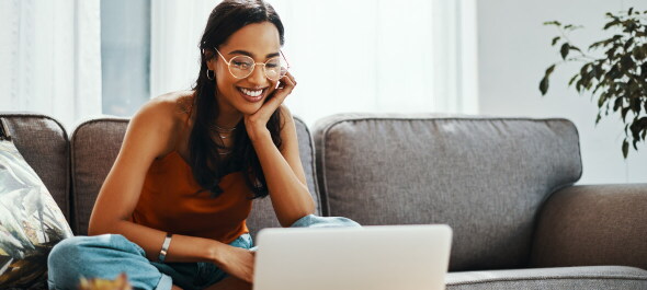 Young female wearing glasses sitting on the sofa with crossed legs on her laptop
