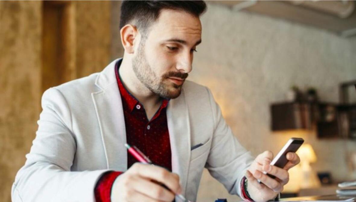 A man looking at his mobile phone and writing