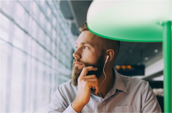 man with beard looking out the window in a collared shirt wearing earphones
