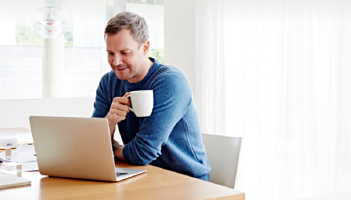 A man drinking from his white cup while looking at his laptop