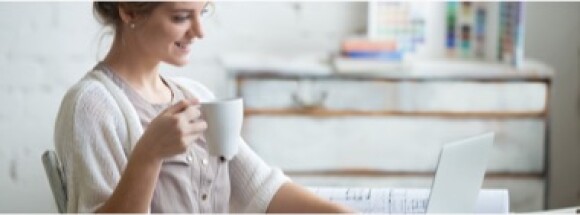 Lady smiling and drinking coffee while using a laptop.
