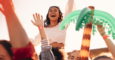 Person lifted above crowd at outdoor event, smiling with hands raised near inflatable palm tree.
