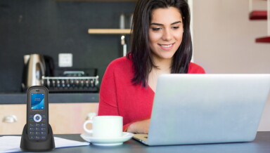 Woman in red shirt using a laptop with a cup of coffee and Home Phone on the table.