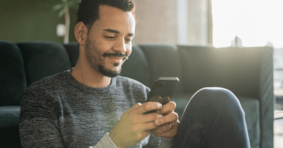 Person sitting down and smiling while looking at a smartphone.