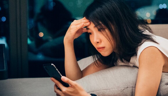 Women holding looking down on phone with the other hand on her forehead thinking