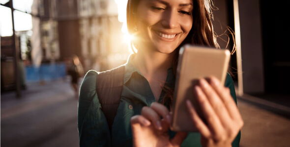 A smiling woman,  leaving work and checking her phone.